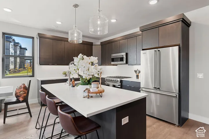 Kitchen featuring dark wood-finish cabinetry, stainless steel appliances, a center island with a light-toned countertop, recessed lighting, and pendant lighting fixtures