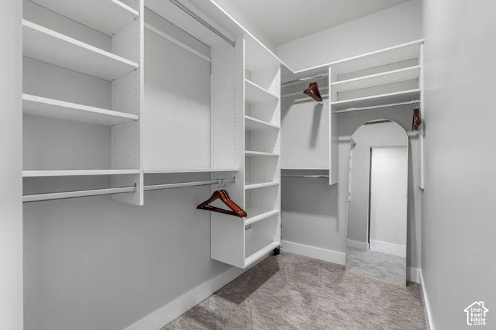 Custom closet system featuring multiple shelving units and hanging rods, light gray wall paint, and gray patterned carpet flooring