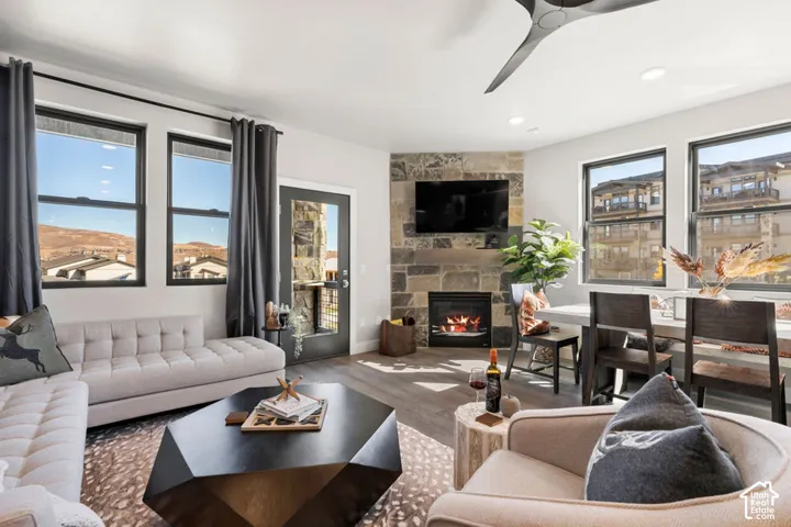 Living space featuring a stone-clad fireplace, wood-finish flooring, recessed lighting, and multiple windows