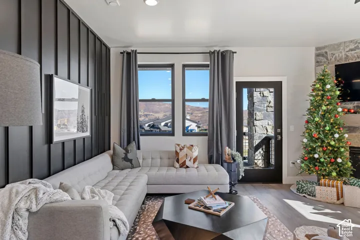 Board and batten accent wall, wood-finish flooring, stone-clad fireplace, large windows, and a glass-paneled door