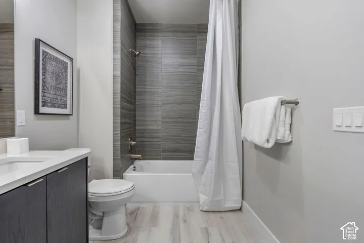 Contemporary bathroom featuring a vanity with integrated sink, dark wood-finish cabinetry, a toilet, a bathtub with a shower, and light wood-finish flooring