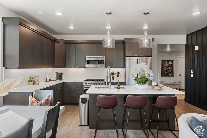 Wood-finish cabinetry, stainless steel appliances, white countertops, kitchen island with seating, and hardwood flooring