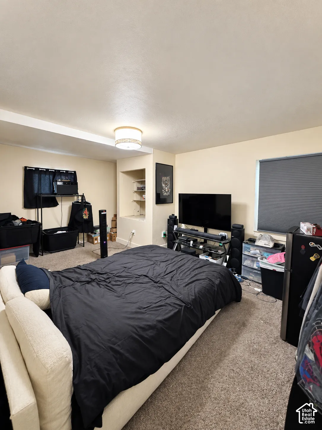 Carpeted room featuring a ceiling-mounted light fixture, recessed wall shelving, and a window with blinds