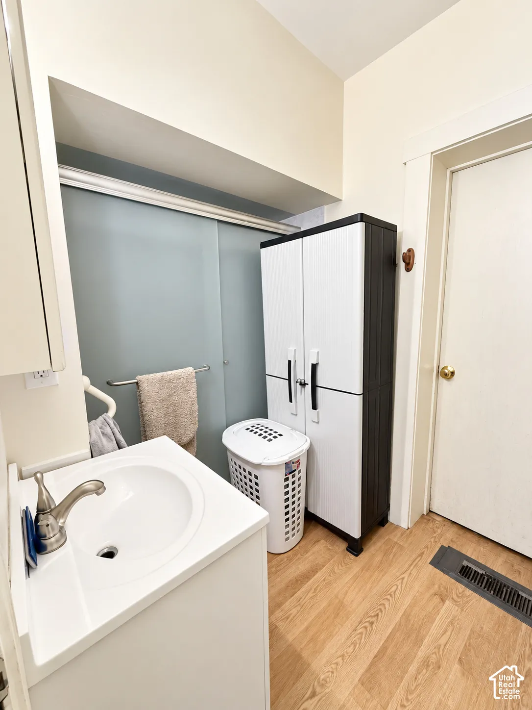 White vanity with integrated sink, brushed nickel faucet, wood-finish flooring, and a sliding glass shower enclosure