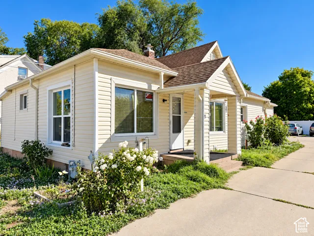 Cream-colored siding exterior, brown shingle roof, covered front porch, multiple windows, and a concrete driveway