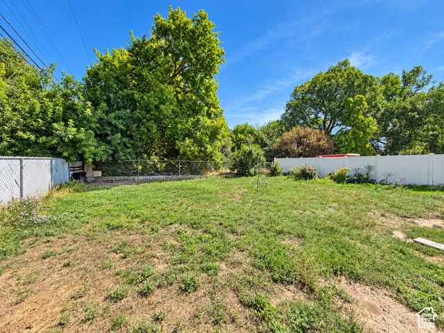 Expansive backyard with a sloped grassy area, partial chain link fencing, and partial white privacy fencing