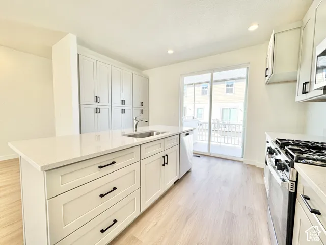 Modern kitchen featuring crisp white cabinetry with shaker-style doors and hardware accents, white quartz countertops with waterfall island edge, stainless steel gas range, and light wood-finish flooring throughout