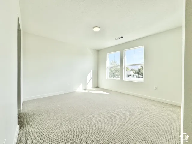 Bright, light-filled bedroom featuring expansive windows with natural illumination, neutral carpet flooring, and clean white walls with recessed ceiling lighting