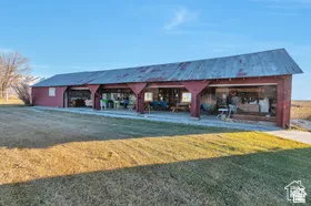 Red barn structure featuring a corrugated metal roof, open bays, and a concrete approach
