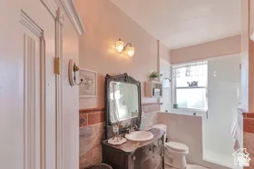 Vanity with ornate mirror, wall-mounted sconce lighting, ceramic tile wainscoting, and a glass-enclosed shower