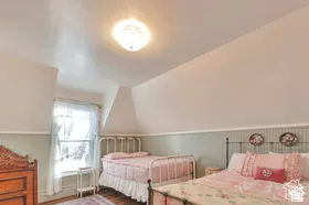 Sloped ceilings with a flush mount light fixture, a window with sheer curtains, wood-finish flooring, and light green wainscoting