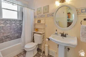 Pedestal sink, wall-mounted mirror, beadboard wainscoting, tiled bath surround, and window