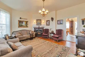 Hardwood flooring, corner fireplace with dark stone surround, decorative chandelier, arched entryway, and wall sconces