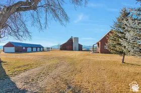 Red barn structures with a prominent silo, a separate multi-bay garage building, and expansive open land
