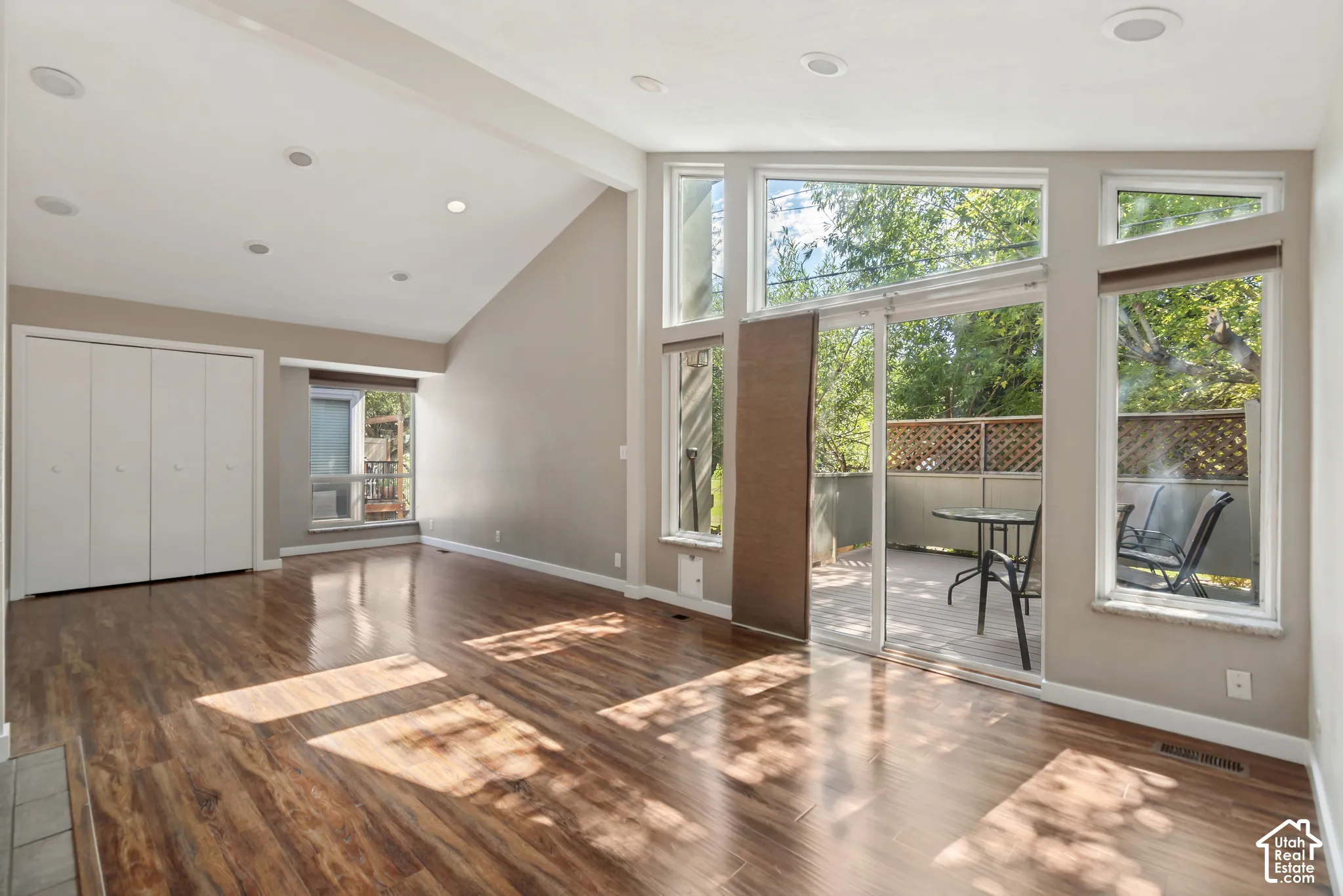 Vaulted ceiling with recessed lighting, wood-finish flooring, sliding glass door to exterior deck, and multiple large windows