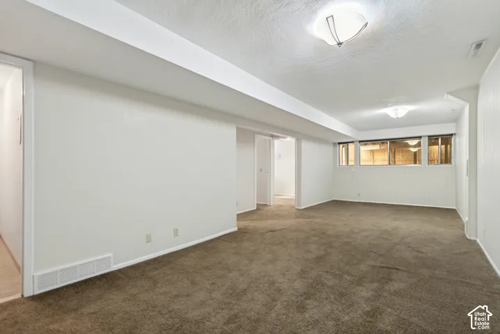 Spacious basement recreation area featuring neutral carpet flooring, abundant natural light from high windows, and multiple rooms with white walls and recessed ceiling lighting