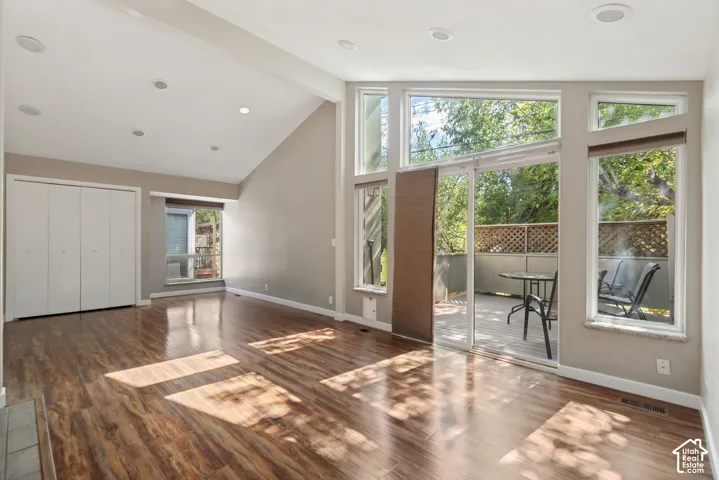 Vaulted ceiling with recessed lighting, wood-finish flooring, sliding glass door to exterior deck, and multiple large windows