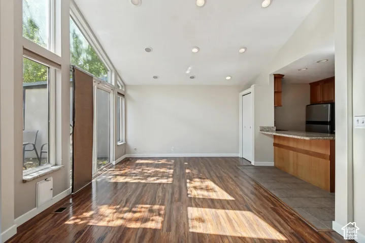 Bright, open living space featuring rich wood-finish flooring, floor-to-ceiling windows with natural light, recessed ceiling lighting, and direct access to a modern kitchen with wood cabinetry and stainless steel appliances