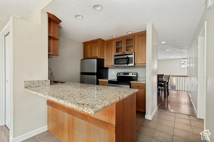 Kitchen featuring granite countertops, stainless steel appliances, wood cabinetry, recessed lighting, and tile flooring