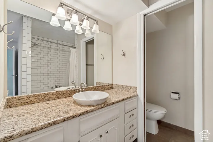 Spa-inspired bathroom featuring a vessel sink set atop warm-toned stone countertops, soft-close cabinetry with brushed nickel hardware, subway tile shower surround with chrome fixtures, and chrome vanity lighting