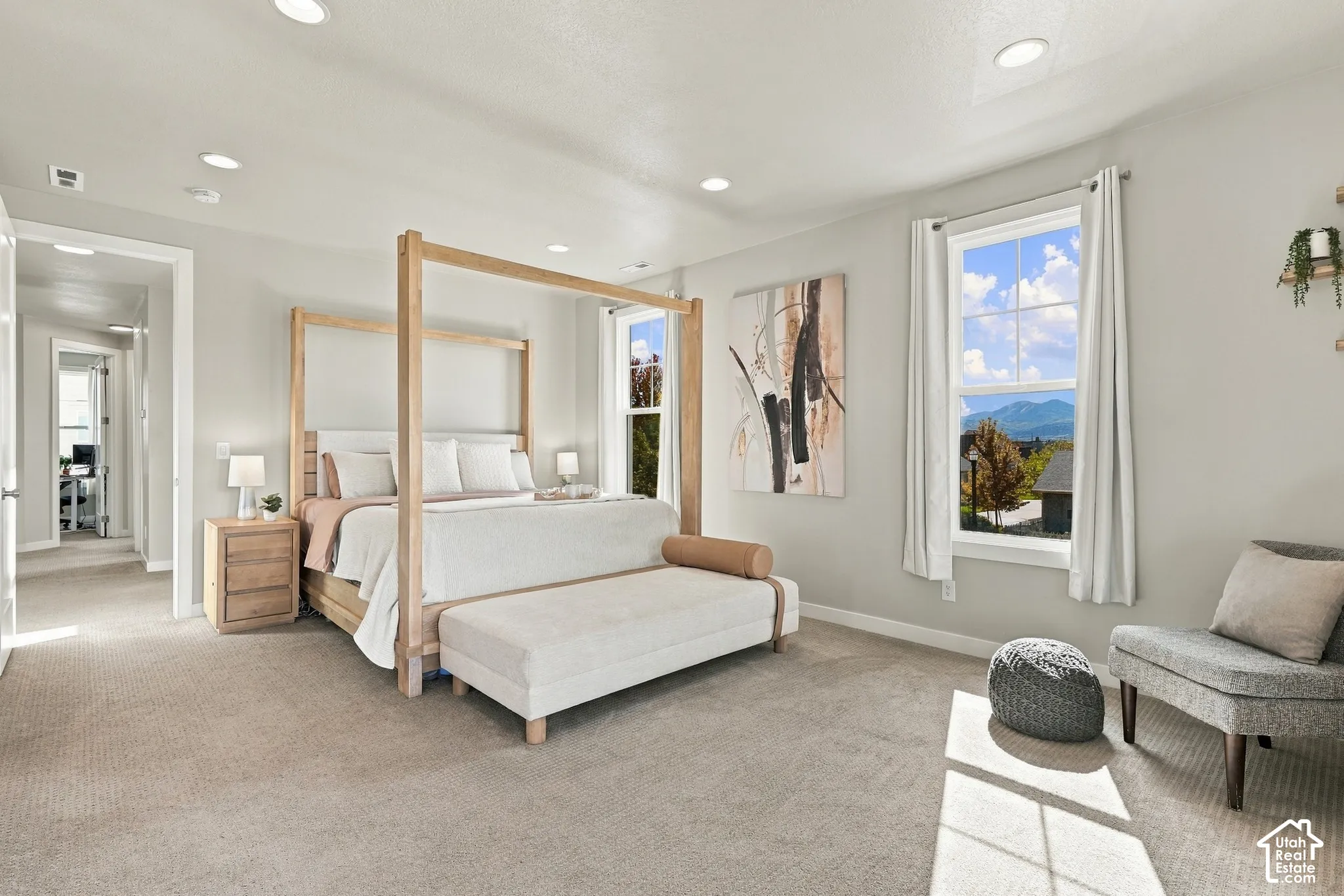 Recessed lighting, light gray wall tones, two large windows, mountain scenery, and light-colored carpet flooring