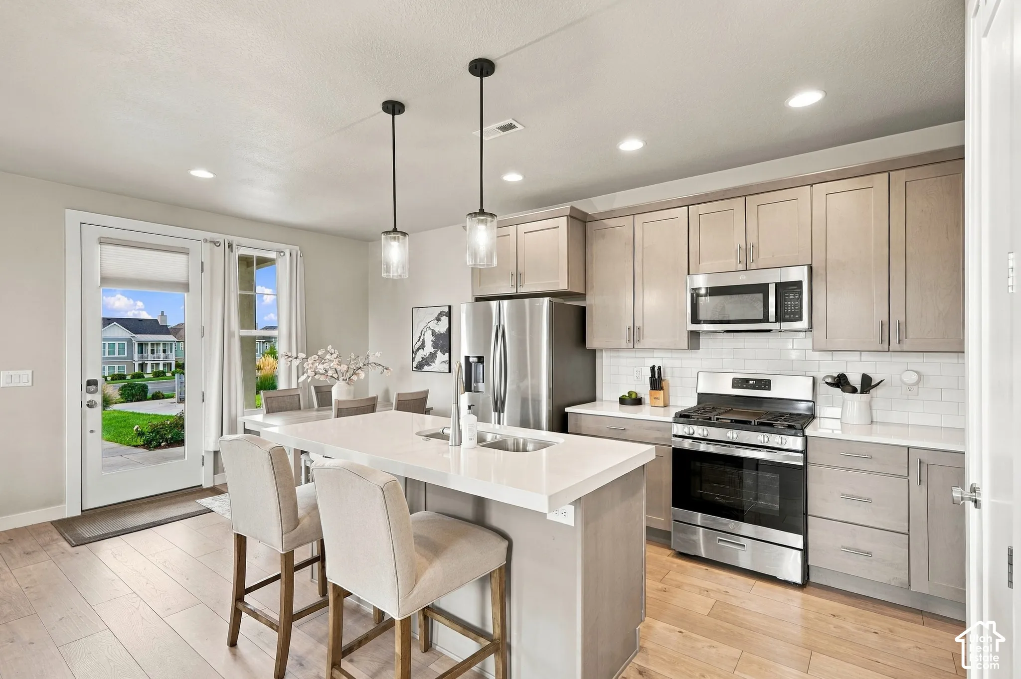 Kitchen featuring wood-finish flooring, an island with countertop seating, stainless steel appliances, a subway tile backsplash, and light-toned cabinetry