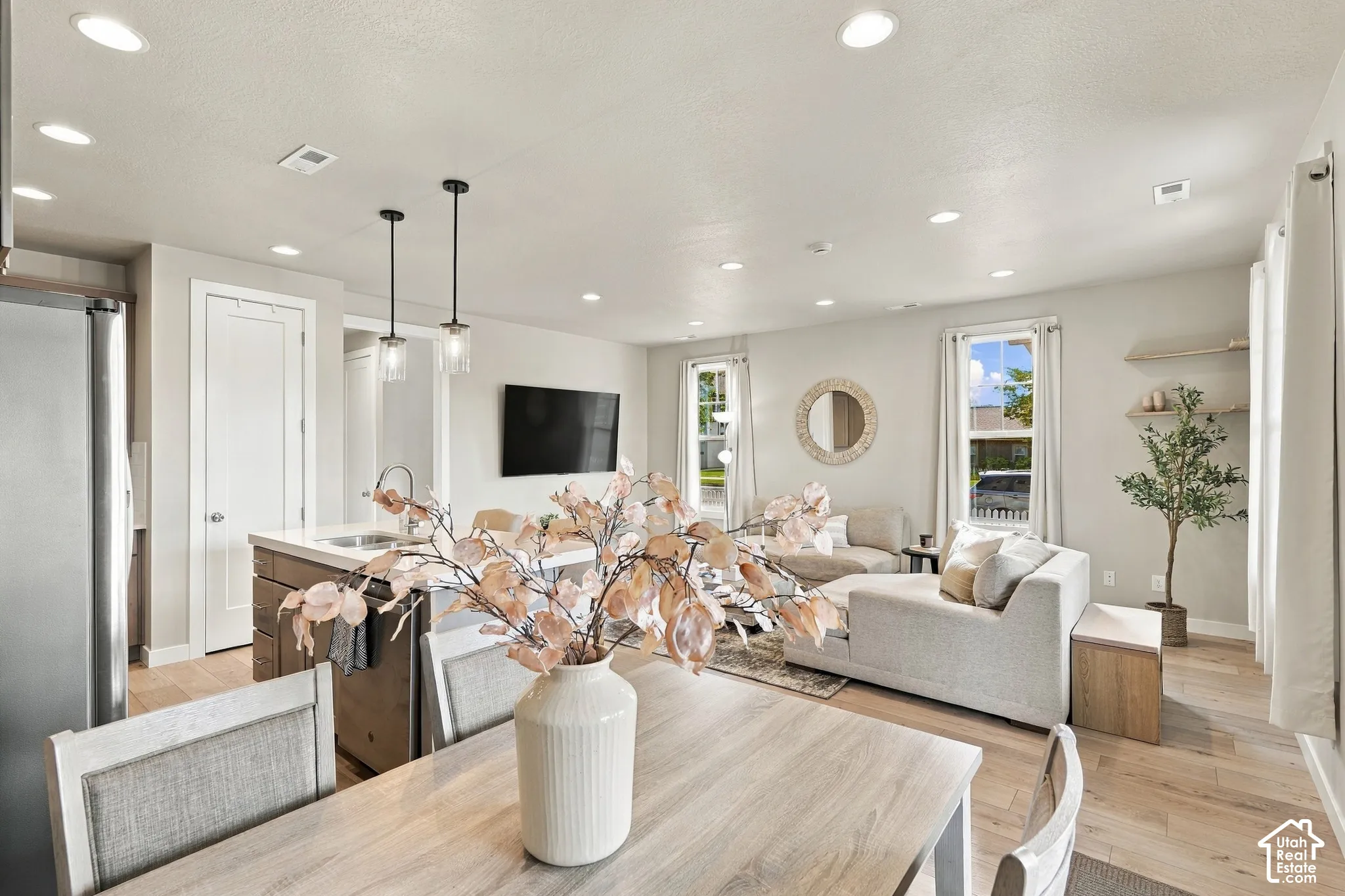 Recessed lighting, wood-finish flooring, two pendant light fixtures, and a kitchen island with a sink