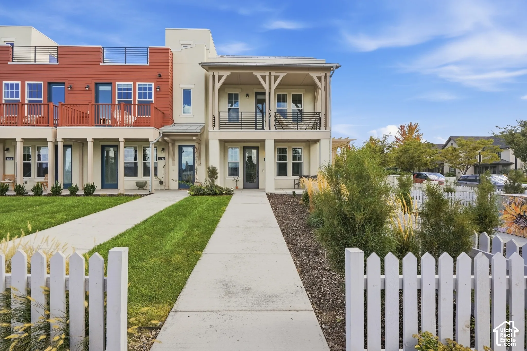 Contemporary townhome featuring a stucco facade, red siding accents, a private balcony with railing, a rooftop terrace, and a white picket fence