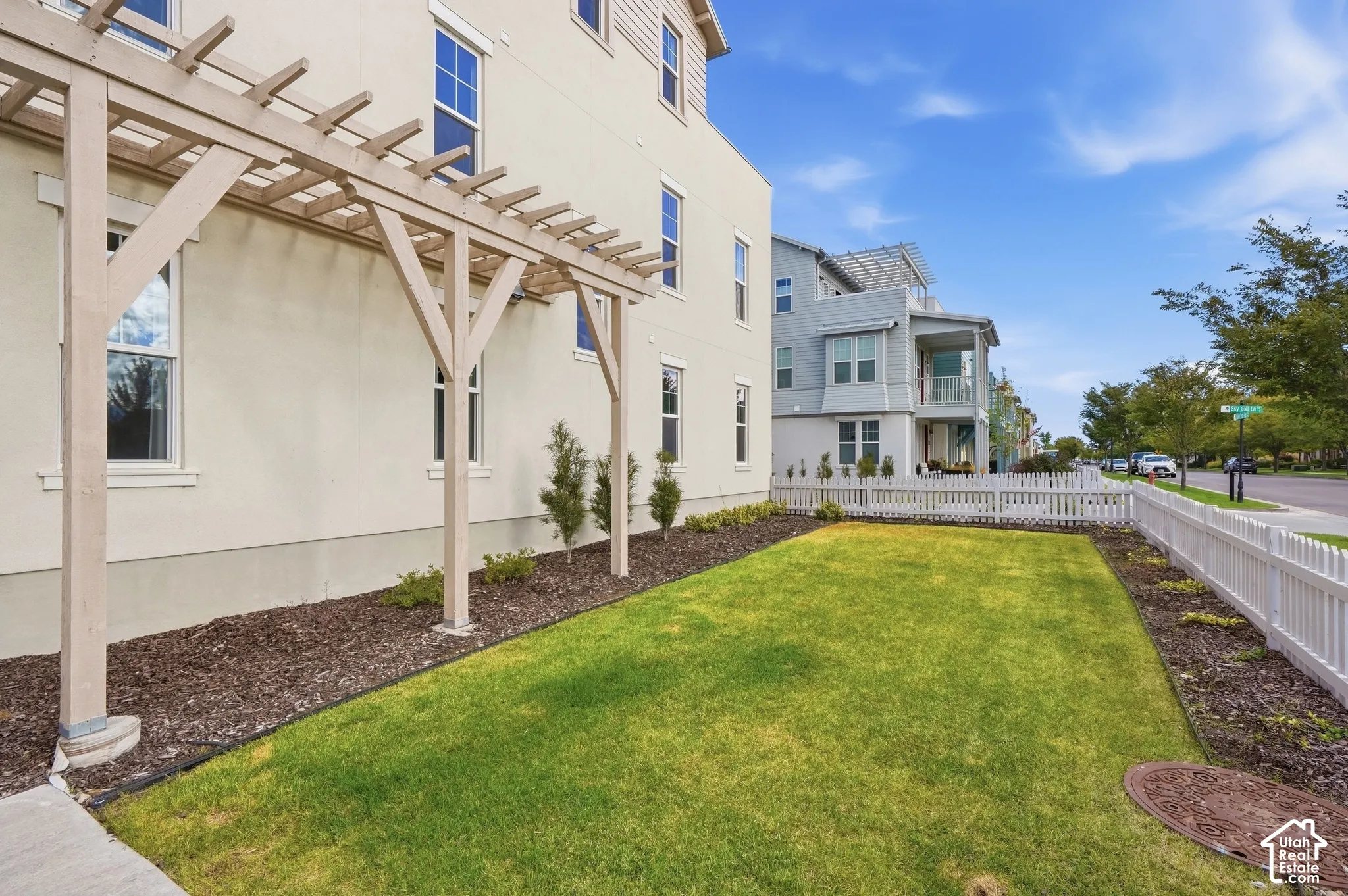 Expansive side yard featuring a manicured lawn, established pergola, white picket fence, and mature trees