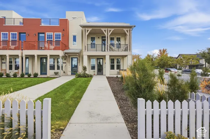 Contemporary townhome featuring a stucco facade, red siding accents, a private balcony with railing, a rooftop terrace, and a white picket fence