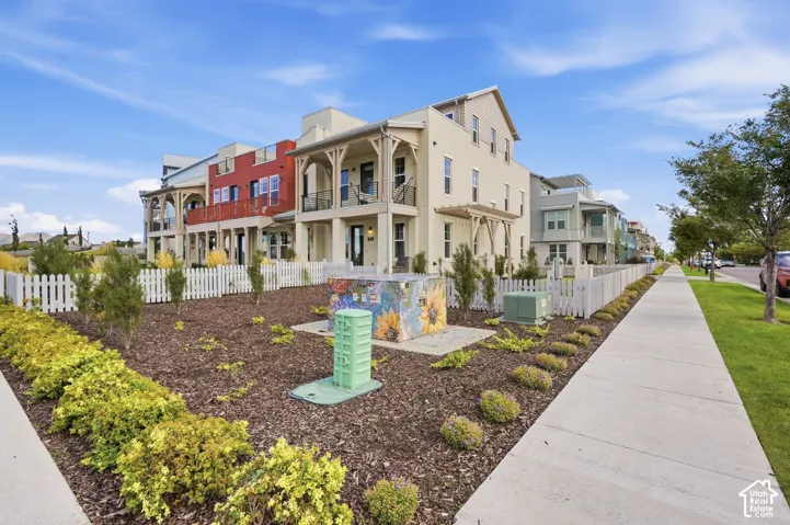 Multi-level townhome with balconies, white picket fencing, and a landscaped front yard