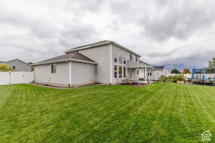 Expansive lawn with a white vinyl fence, covered patio, and a separate storage shed