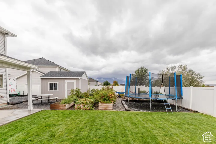 Expansive backyard featuring a manicured lawn, a detached storage shed, raised garden beds, and a white privacy fence