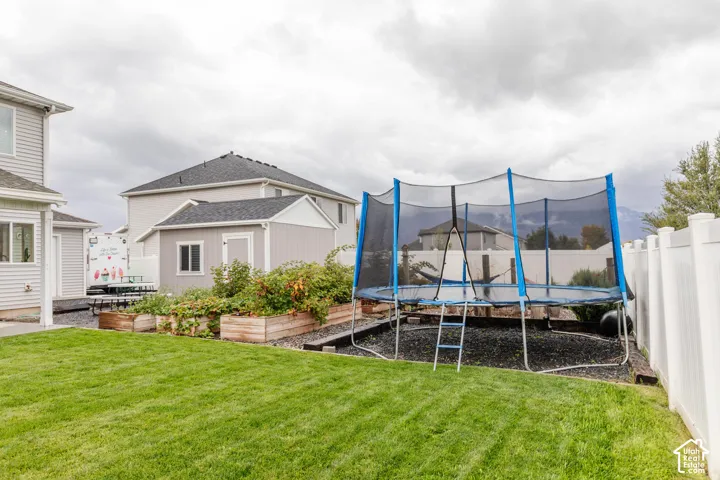 Expansive green lawn, white vinyl fencing, detached storage shed, and raised garden beds