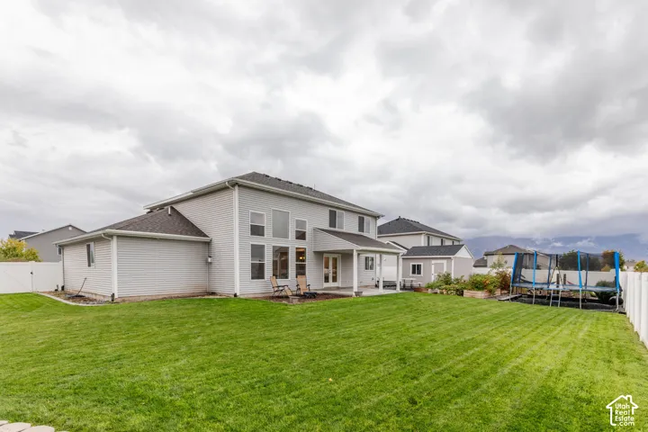 Expansive rear yard featuring a manicured lawn, white vinyl fencing, and a covered concrete patio