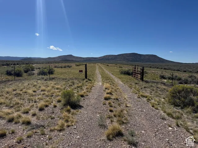 Expansive undeveloped land featuring a gravel road, wire fencing, and a metal gate, with distant mountains under a clear sky