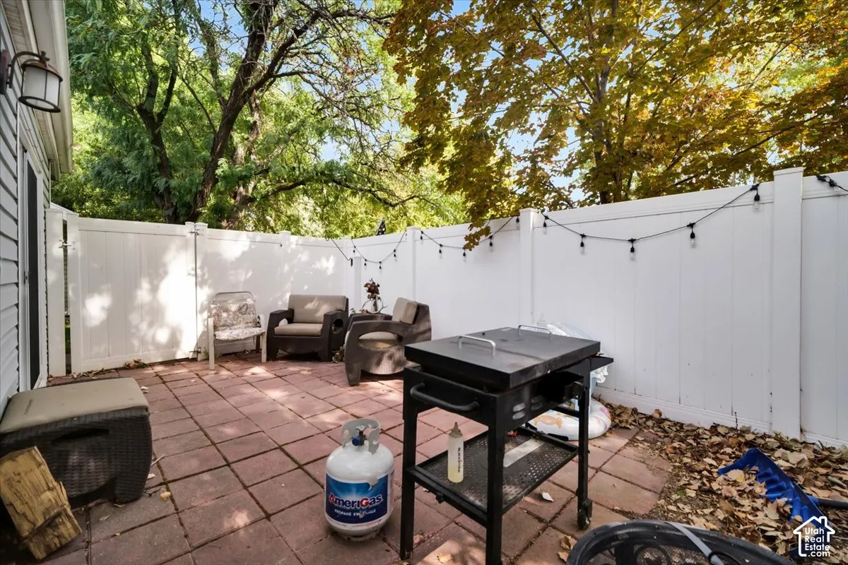 Paved patio area featuring white fencing, string lighting, and mature trees