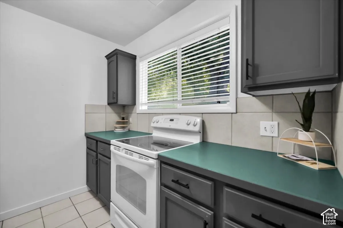 Tile flooring with dark gray cabinetry, teal countertops, and a white electric range