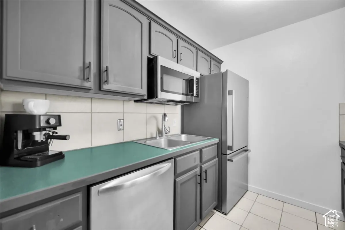 Gray cabinetry with black hardware, stainless steel dishwasher, stainless steel microwave, stainless steel refrigerator, and a tile backsplash
