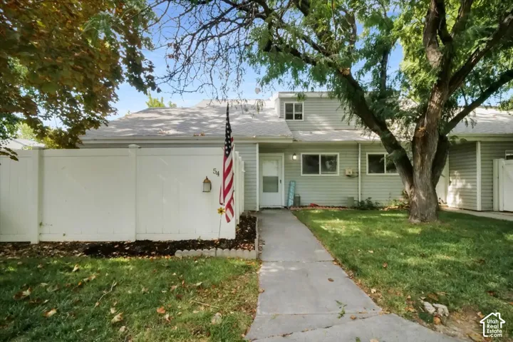 Exterior featuring light-toned siding, a concrete pathway, a privacy fence, and mature trees