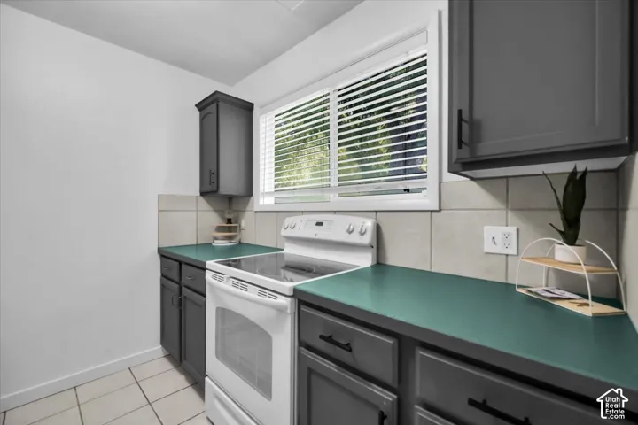 Tile flooring with dark gray cabinetry, teal countertops, and a white electric range