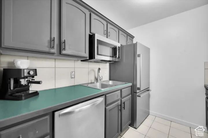 Gray cabinetry with black hardware, stainless steel dishwasher, stainless steel microwave, stainless steel refrigerator, and a tile backsplash