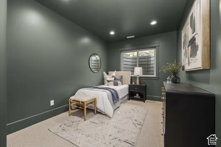 Recessed lighting illuminates a space featuring a window with a well-cover, carpet flooring, and dark-toned walls