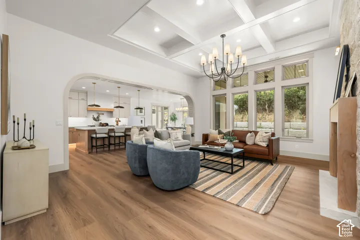 Coffered ceiling with an elegant chandelier, expansive windows, wood-finish flooring, and a stone fireplace with a light wood mantel