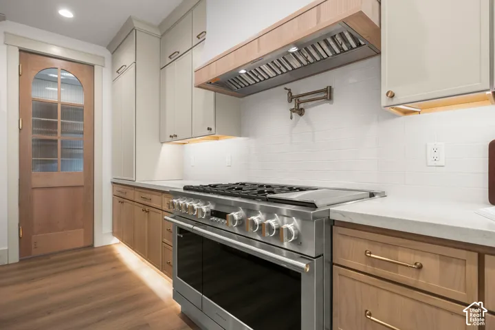 Stainless steel range, wood-finish flooring, white subway tile backsplash, light-toned upper cabinetry, and natural wood lower cabinetry