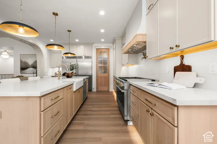 Gourmet kitchen featuring a farmhouse sink, stainless steel appliances, wood-finish flooring, white subway tile backsplash, and two-tone cabinetry