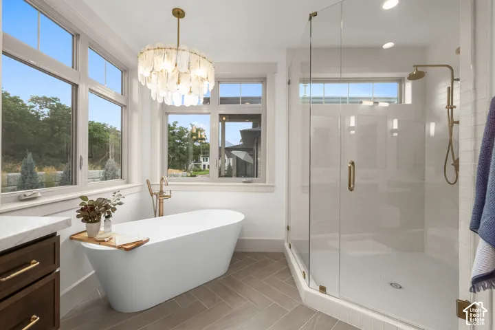 Freestanding soaking tub with a floor-mounted brass faucet, glass-enclosed shower, wood-finish flooring in a herringbone pattern, and a decorative chandelier