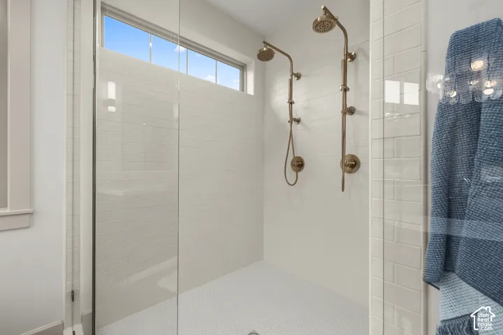 Glass-enclosed shower with dual shower heads, white subway tile walls, a mosaic tile floor, and a transom window