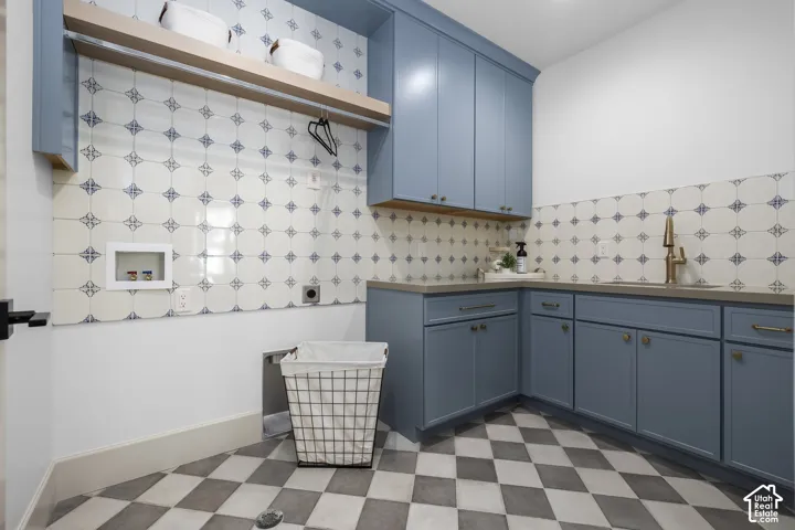 Blue cabinetry with brass hardware, patterned tile backsplash, light wood shelving, neutral countertops, and checkerboard floor tile