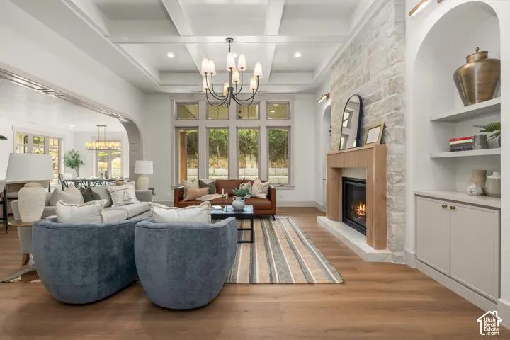 Coffered ceiling, wood-finish flooring, stone-clad fireplace with wood mantel, arched built-in shelving, and transom windows